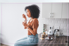 Woman sitting on kitchen worktop and eating a probiotic yoghurt